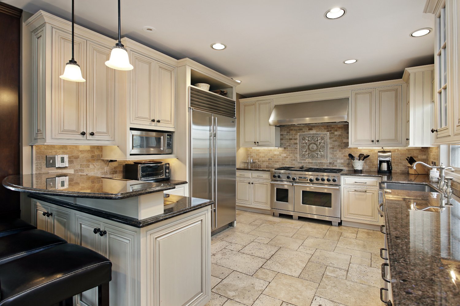 Upscale peninsula kitchen with white cabinets, dark marble countertops and breakfast bar 